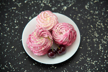 Close up of pink marshmallows with sweet cherries in a white plate. Black background.