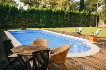 Garden with green grass with wooden tables and chairs, with a pool in the background