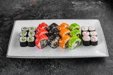 set of rolls and sushi on a white plate on a black textured background decorated with soy sauce and spices