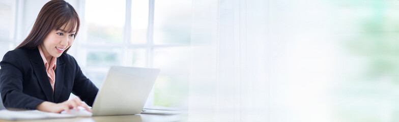 Beautiful Asian business woman wore a black suit sitting in the office, smiling happily. Asian business women for banner and background.