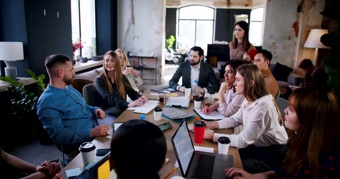 Teamwork concept. Young male coach speaking to multiethnic business team at modern loft office meeting slow motion.