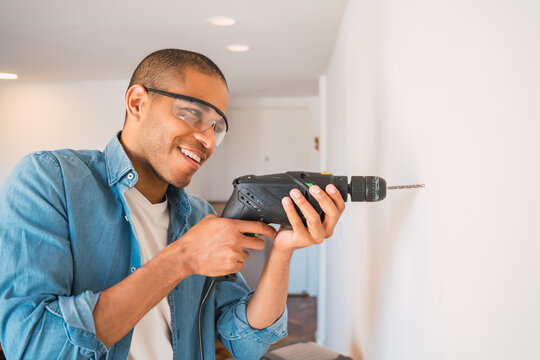 Young man with a electric drill and making hole in wall.