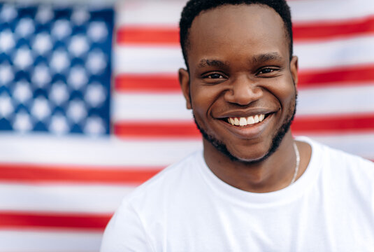 Close-up portrait of attractive smiling african american guy in a white t-shirt whos stands on USA flag background