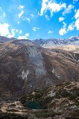 A small lake hiding under harsh and golden colored slopes in Manang Valley, Himalayas, Nepal. Dry and desolated landscape. The lake has dark green color. Serenity and peace of mind