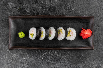 Sushi California Roll with crab meat, cucumber, masago, chopsticks on a gray plate, black background, side view