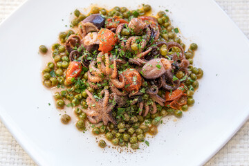 Octopus, peas and tomato. Ready to eat. Small octopuses cooked with cherry tomatoes, oil and peas. Tasty dish of Italian cuisine served on white plate.