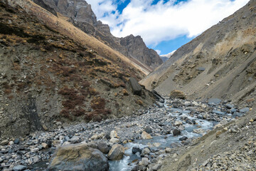 A view on rushing brook in Manang Valley, Annapurna Circus Trek, Himalayas, Nepal, with  Annapurna Chain and Gangapurna in the back. Dry and desolated landscape. High, snow capped mountain peaks.