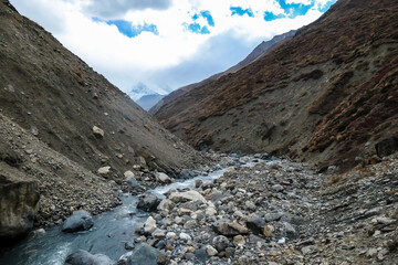 A view on rushing brook in Manang Valley, Annapurna Circus Trek, Himalayas, Nepal, with  Annapurna Chain and Gangapurna in the back. Dry and desolated landscape. High, snow capped mountain peaks.