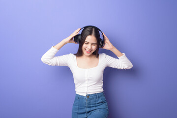 Fototapeta na wymiar Young woman is listening to music on purple background