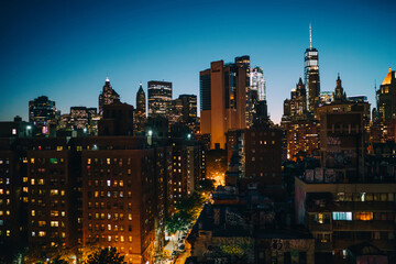 Obraz premium Urban setting at dusk with tall architecture construction shining with window lights; New York big city life in evening with skyscrapers and towers for rental real estate in district of megalopolis