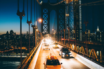 Metropolitan traffic on Brooklyn bridge with vehicles shining with evening light, yellow cab taxis...