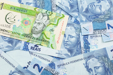 A one manat bank note from Turkmenistan close up in macro with an assortment of Brazilian two reais bank notes.