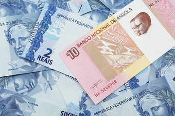 An red and white ten Angolan kwanza bank note on a background of Brazilian two reais bank notes