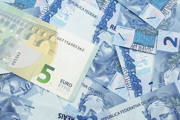 A close up image of a five Euro bank note from Europe in macro with a bed of Brazilian two reais bank notes