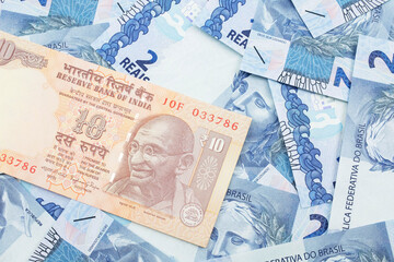 A close up image, shot in macro, of an orange, ten rupee Indian bank note on a bed of blue, two Brazilian real notes