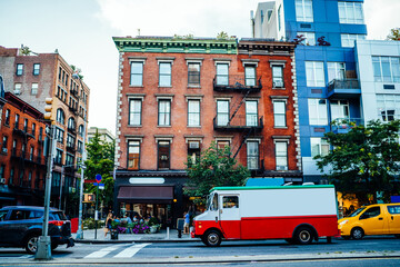Vintage building exterior in residential district and truck of delivery service driving on road for relocation; traffic on avenue near old architecture with stores and flats in megapolis