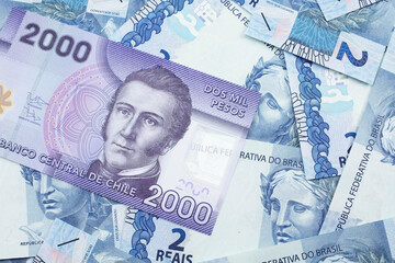 A close up image of a purple two thousand peso bank note from Chile on a bed of Brazilian two reais bank notes in macro
