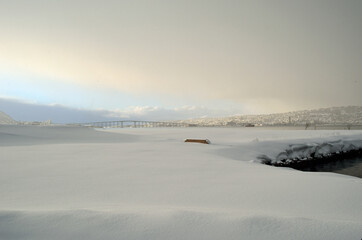 Obraz premium blue sky over fjord and tromsoe city island and bridge with snow heavy clouds