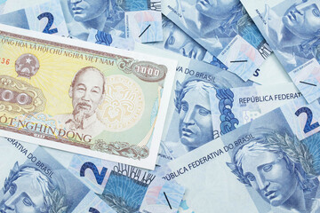 A close up image of a Vietnamese one thousand dong bank note on a background of Brazilian two reais bank notes in macro