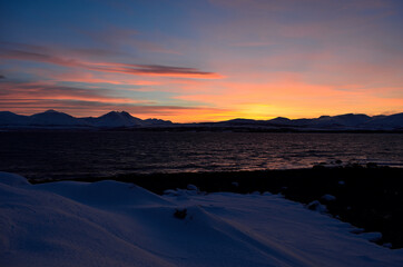 red vibrant sunset sky over snowy mountain and fjord