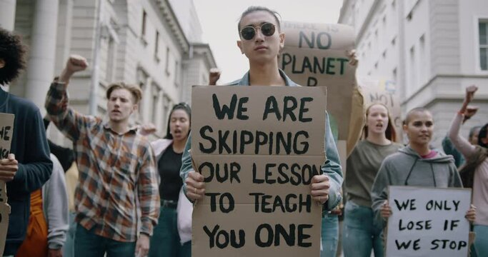 Young student holding poster with "we are skipping out lesson to teach you one". Group of demonstrators making protest about climate change.
