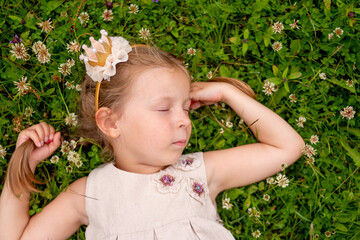 Sweet little girl sleeping on a green grass. girl lying on the grass. child relaxating outdoor.Cute girl lies on her back on the green grass lawn in near country house, relaxing and meditating in