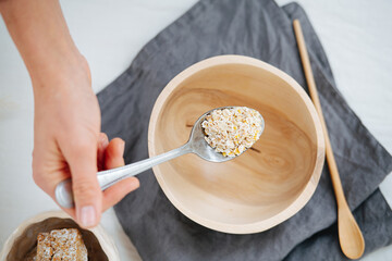 Woman holding spoonful of oat over a wooden bowl on a napkin on a white surface
