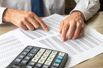 Businessman Analyzing Accounting financial Documents With Calculator on foreground At Desk In Office