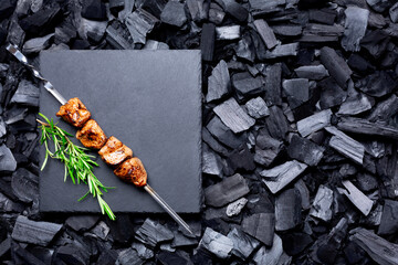 Cooked meat on skewer and a rosemary branch on a black coal background. Barbecue concepе. copy space