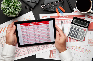 Top view of businessman's hands working with tablet pc and financial reports. Modern black office desk with notebook, pencil and a lot of things. Flat lay table layout.