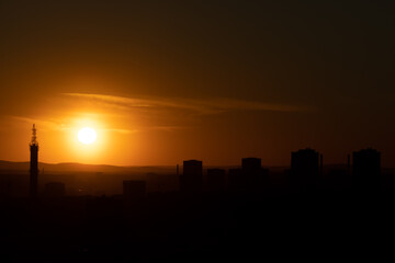 Fototapeta premium Black silhouettes of buildings are on a red sky background with orange and yellow sunset