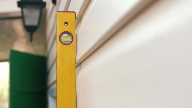 Close-up using a yellow level tool, a builder measures the plane of a wall in a house under construction. Suburban construction and archeology