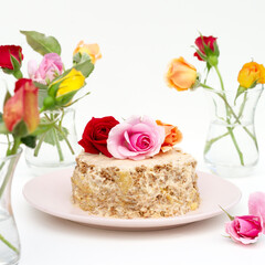 Obraz na płótnie Canvas Homemade little cake decorated with live roses on a white background. Multi-colored roses stand in a glass armudu on the table.