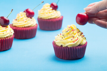 Cupcakes with whipped cream and woman's hand decorating with a cherry made without lactose