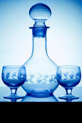 Empty crystal alcoholdecanter and two glasses for vodka standing on a glass table. Vertical side view, cold tone