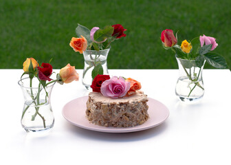 Homemade little cake decorated with live roses on a white background. Multi-colored roses stand in a glass armudu on the table.
