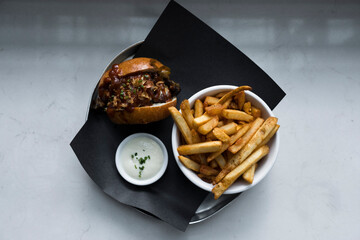BBQ pulled pork sandwich with fresh cut fries and aioli. White marble background. 