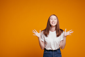 Red-haired girl in a white T-shirt gesticulates with her hands and laughs with all her mouth rejoicing at discounts or a sudden surprise on an orange background