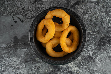 Tasty bacon wrapped onion rings on black plate over blue stone background with free space. Top view, flat lay