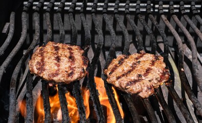 2 hamburgers sizzling on flaming barbecue grill