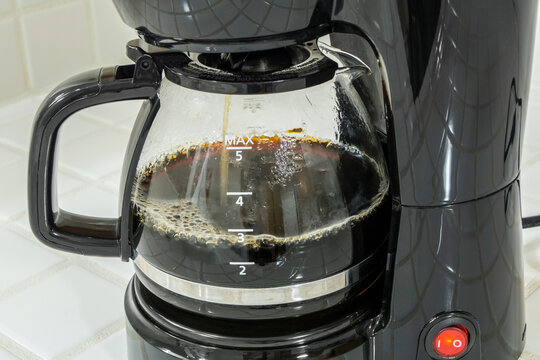 Close up of coffee maker filling pot with fresh brewed caffeine.