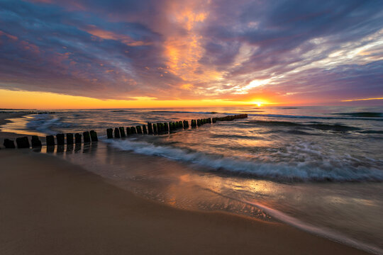 beautiful sunset on the Baltic Sea, waves washing the old wooden breakwaters - Powered by Adobe