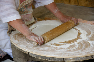 A woman rolls dough to make lavash (a traditional flatbread) which will then be baked in a tandoor...