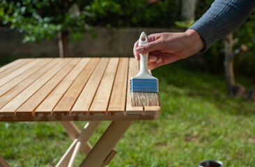 Close-up of a woman's hand coating a garden table with a brush and protective varnish