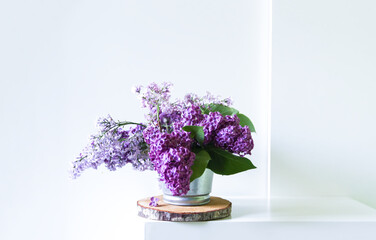 Bouquet of the beautiful spring purple lilac flowers on light background. Common Syringa plant. Natural decor. Floral composition on wooden slice in minimalist light interior.
