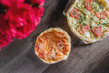 Appetizing pizza on a wooden table, on a tray, with a bouquet of roses. The concept of food and pastime