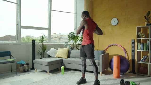 Sportive young fit african man doing upper body twists exercises warming up before fitness workout at home. Activity, sports, health lifestyle.