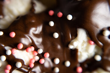 macro photo white ice cream poured with chocolate topping with sprinkles.