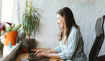 Smiling girl is typing something on her laptop a work desk with plants