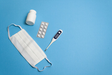 Concept protective equipment against pandemic, coronavirus, top view. Medical, hygiene face mask, tablet plate, pills, capsule bottle, thermometer on blue background, isolated. Blank space for text